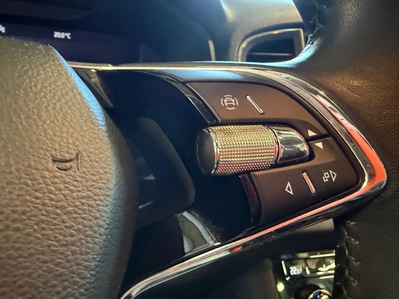 Gros plan sur les commandes au volant côté gauche du Skoda Karoq blanc 2023, avec molette métallique et boutons noirs.