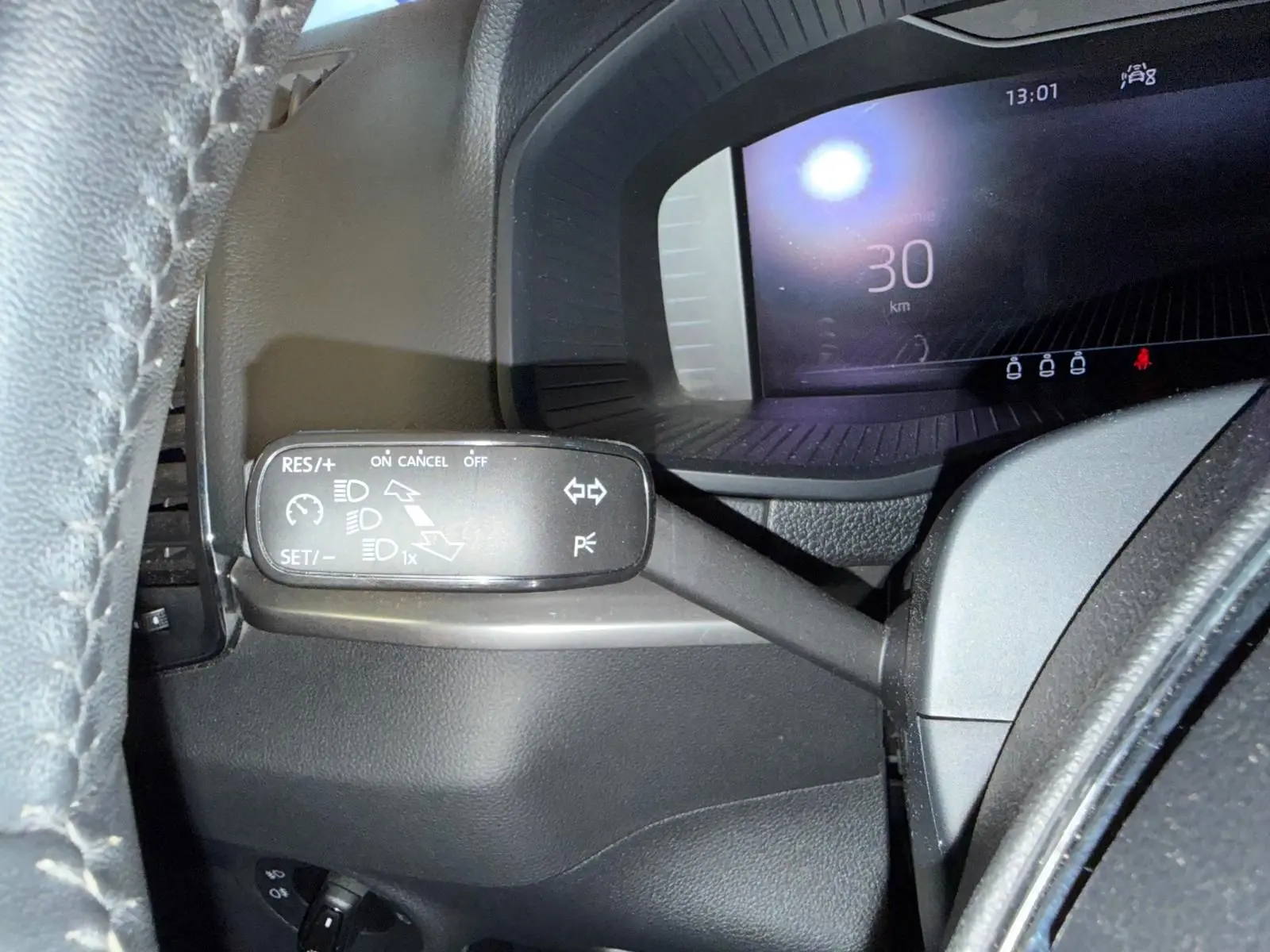 Gros plan sur la manette de régulateur de vitesse à gauche du volant du Skoda Karoq blanc, tableau de bord numérique en arrière-plan.