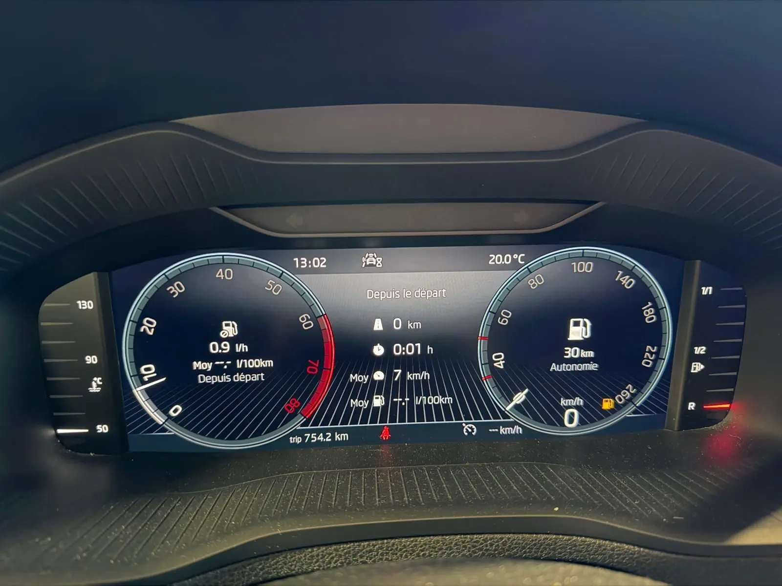 Tableau de bord numérique du Skoda Karoq blanc 2023, affichant vitesse, consommation et autonomie essence.