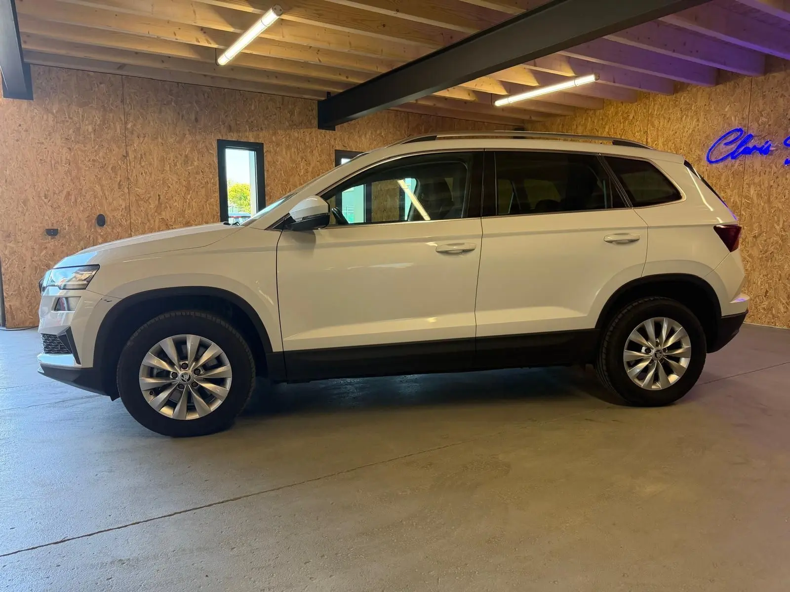 Vue de profil côté gauche d'un Skoda Karoq blanc 2023 avec jantes alliage, stationné en intérieur.