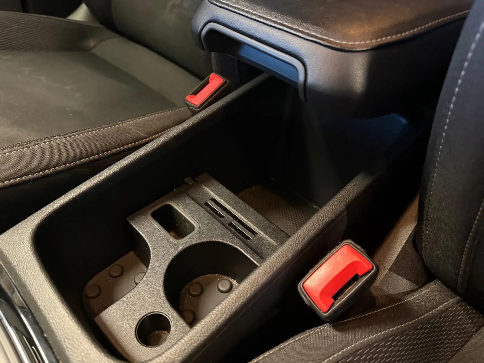 Gros plan sur la console centrale noire avec porte-gobelets et ceintures de sécurité rouges du Skoda Karoq 2023.