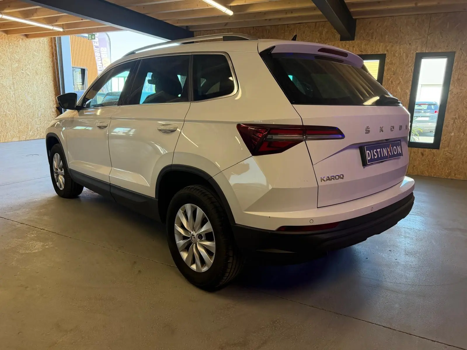 Vue 3/4 arrière droite d'un Skoda Karoq blanc 2023 avec jantes alliage et logo distinctif sur hayon.