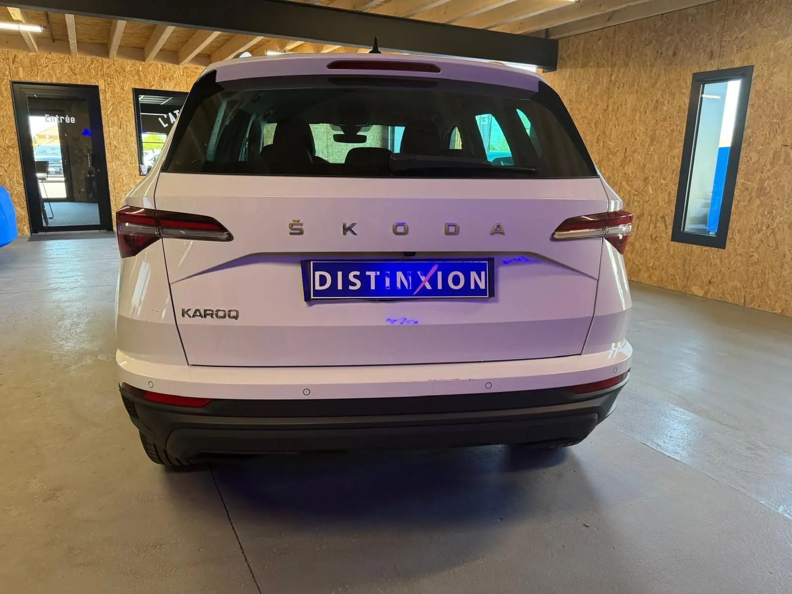 Vue arrière d'un Skoda Karoq blanc 2023 avec logo ŠKODA et plaque Distinxion dans un garage.