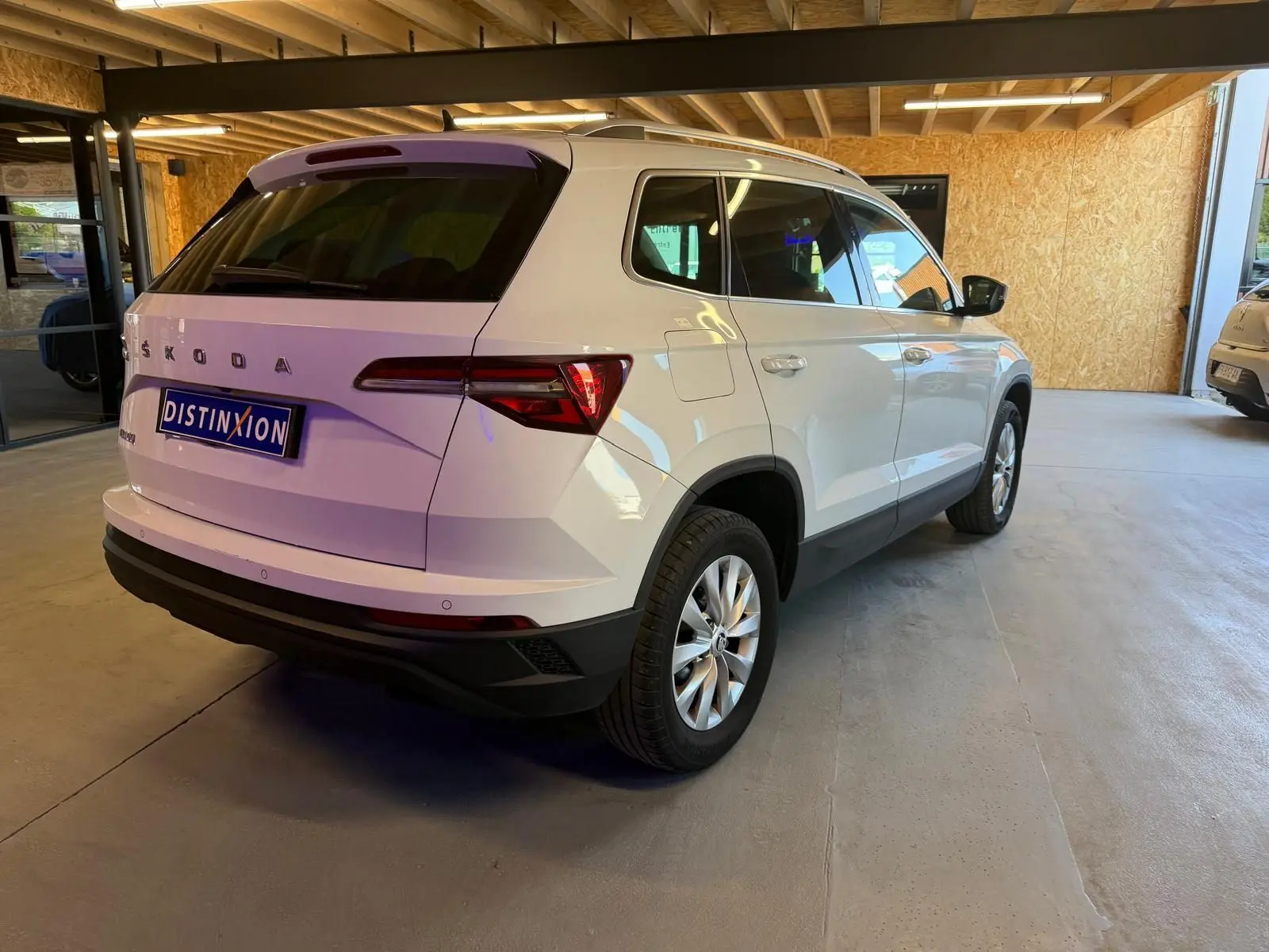 Vue 3/4 arrière droite d'un Skoda Karoq blanc 2023, avec feux arrière LED et jantes alliage, stationné en intérieur.