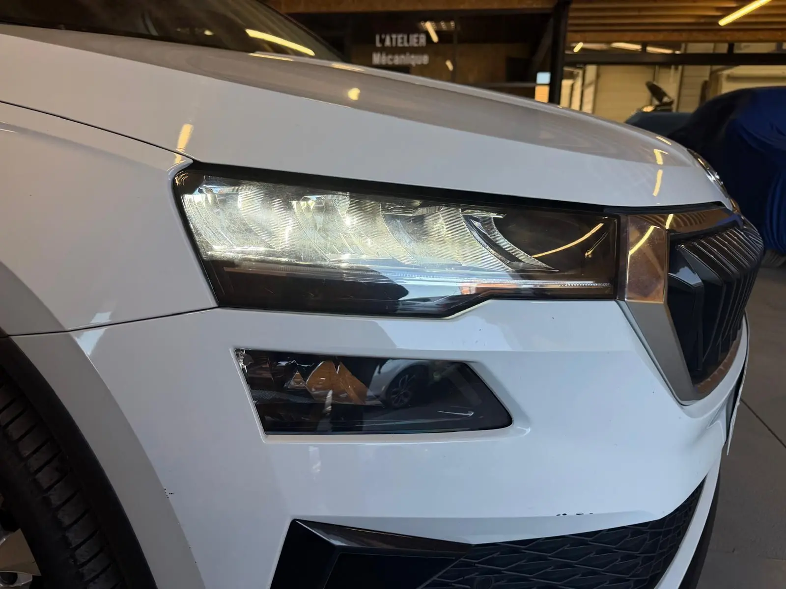 Gros plan sur l'avant gauche blanc du Skoda Karoq 1.5 TSI 150 Ambition 2023, mettant en valeur le phare et la calandre.