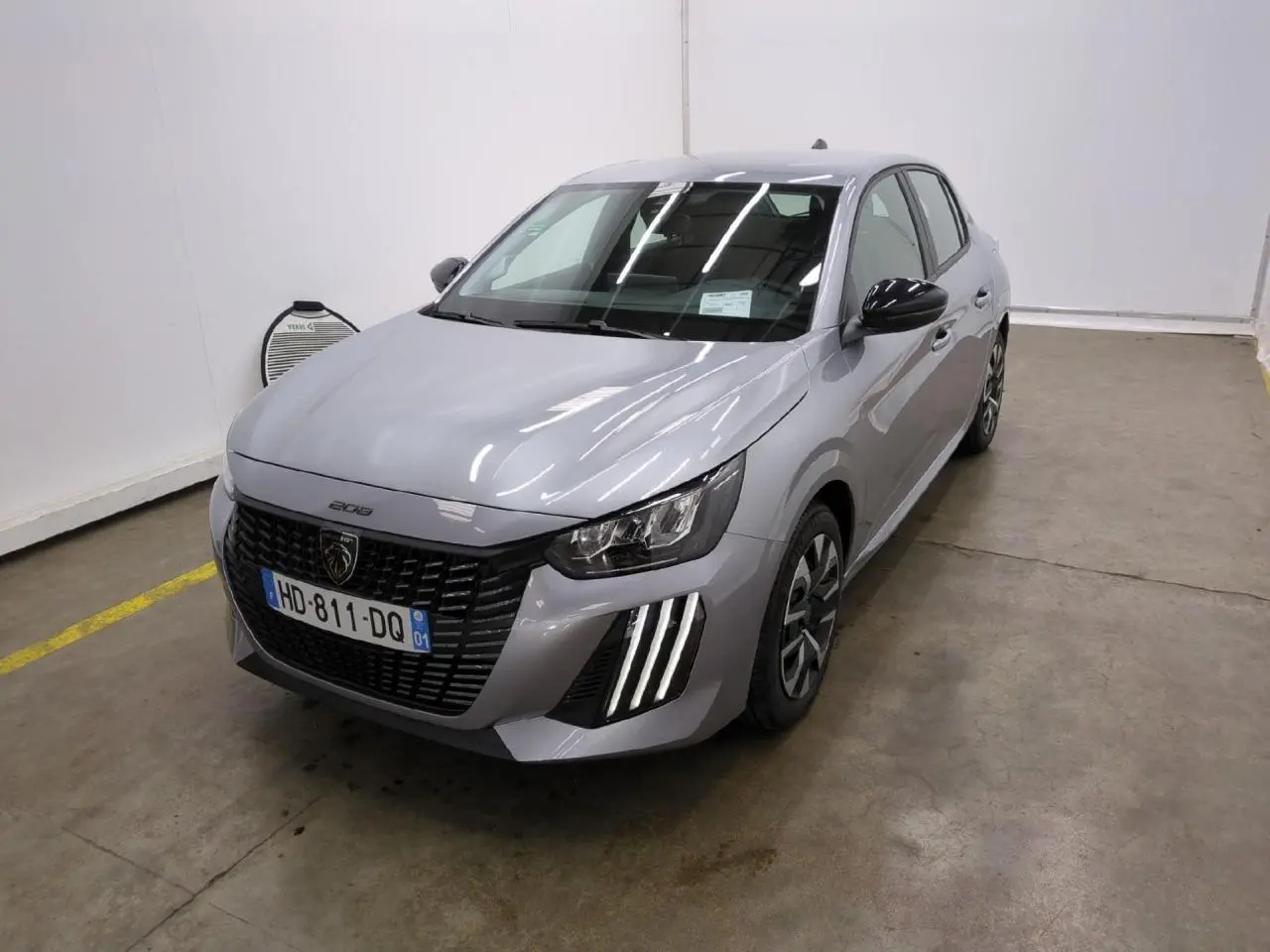 Peugeot 208 gris clair vue 3/4 avant droit avec calandre noire et feux LED signature 3 griffes.