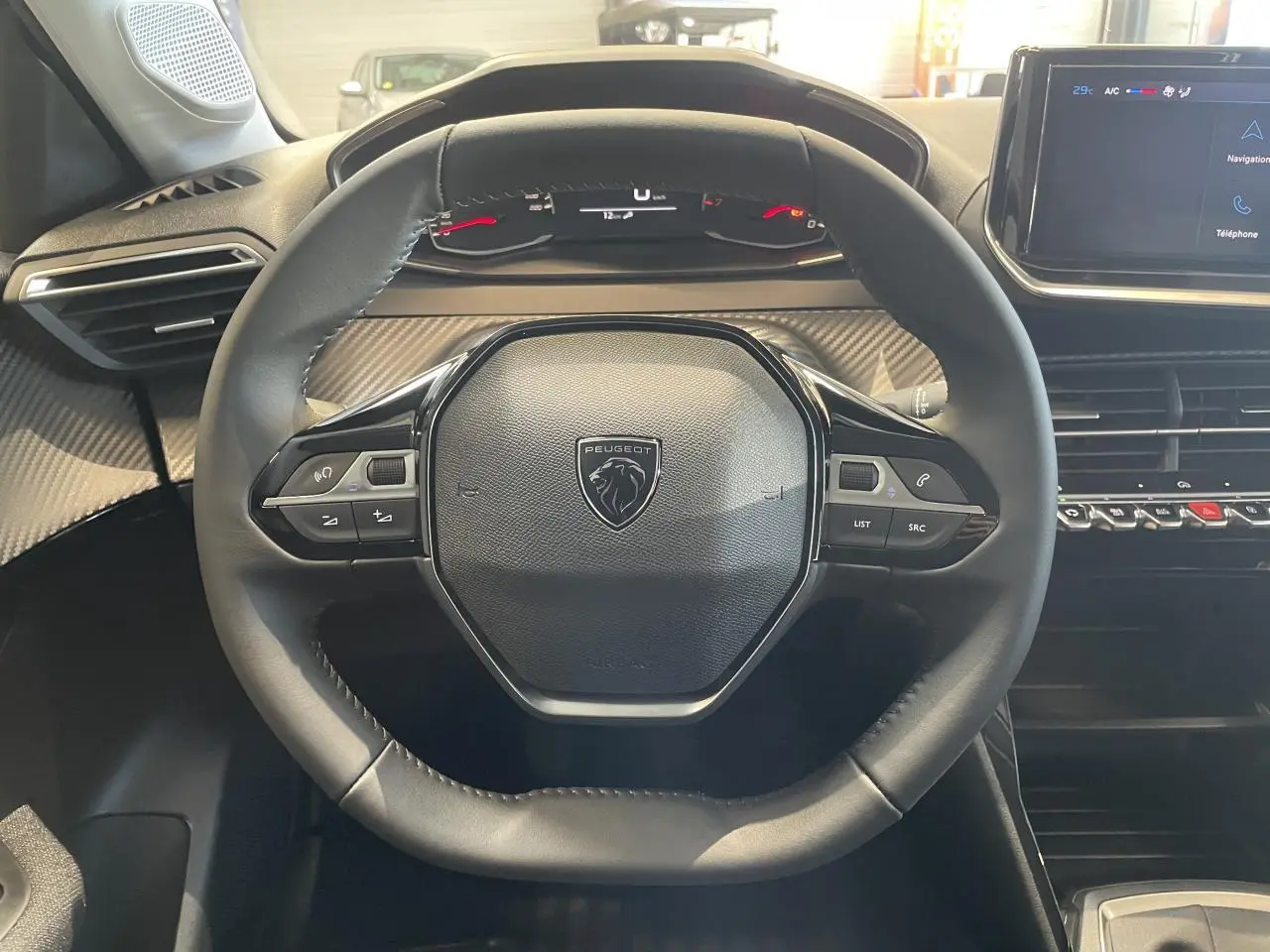 Vue intérieure centrée sur le volant cuir noir de la Peugeot 208 2025 avec tableau de bord et écran tactile.