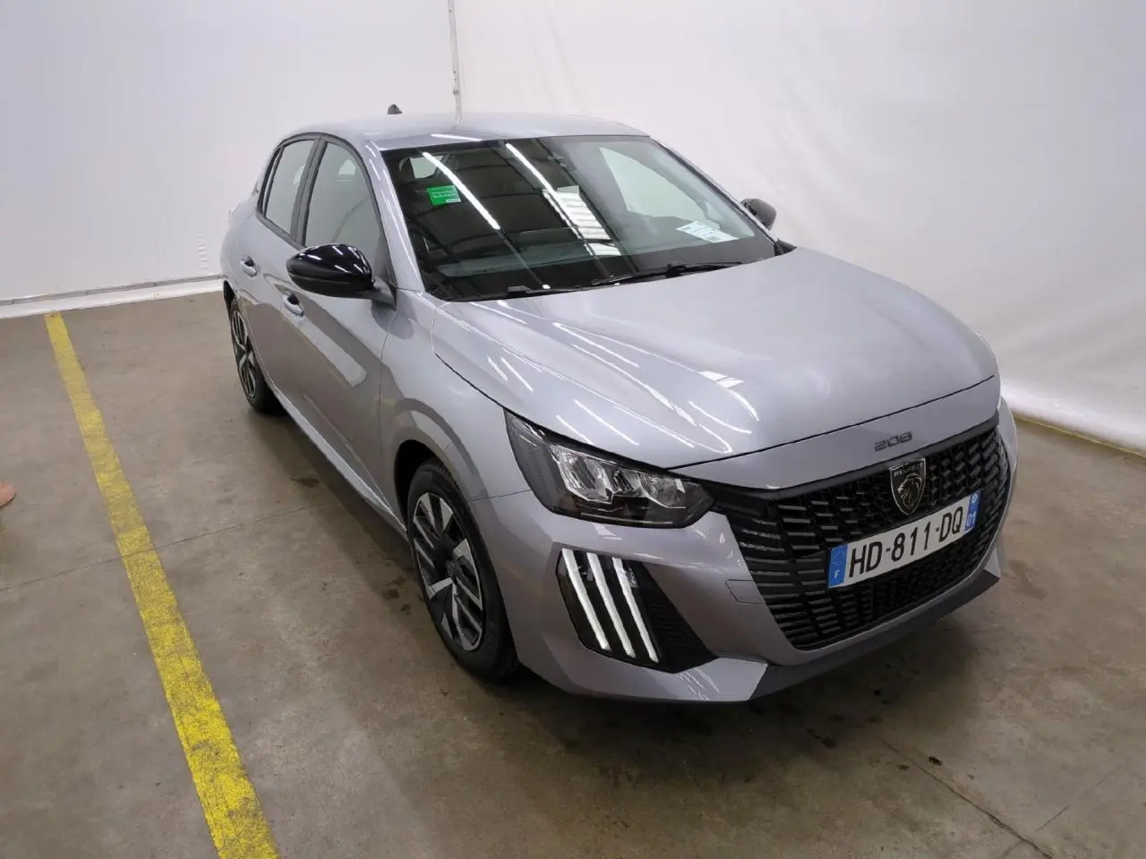 Peugeot 208 gris clair vue 3/4 avant droit avec calandre noire et feux LED signature 3 griffes.