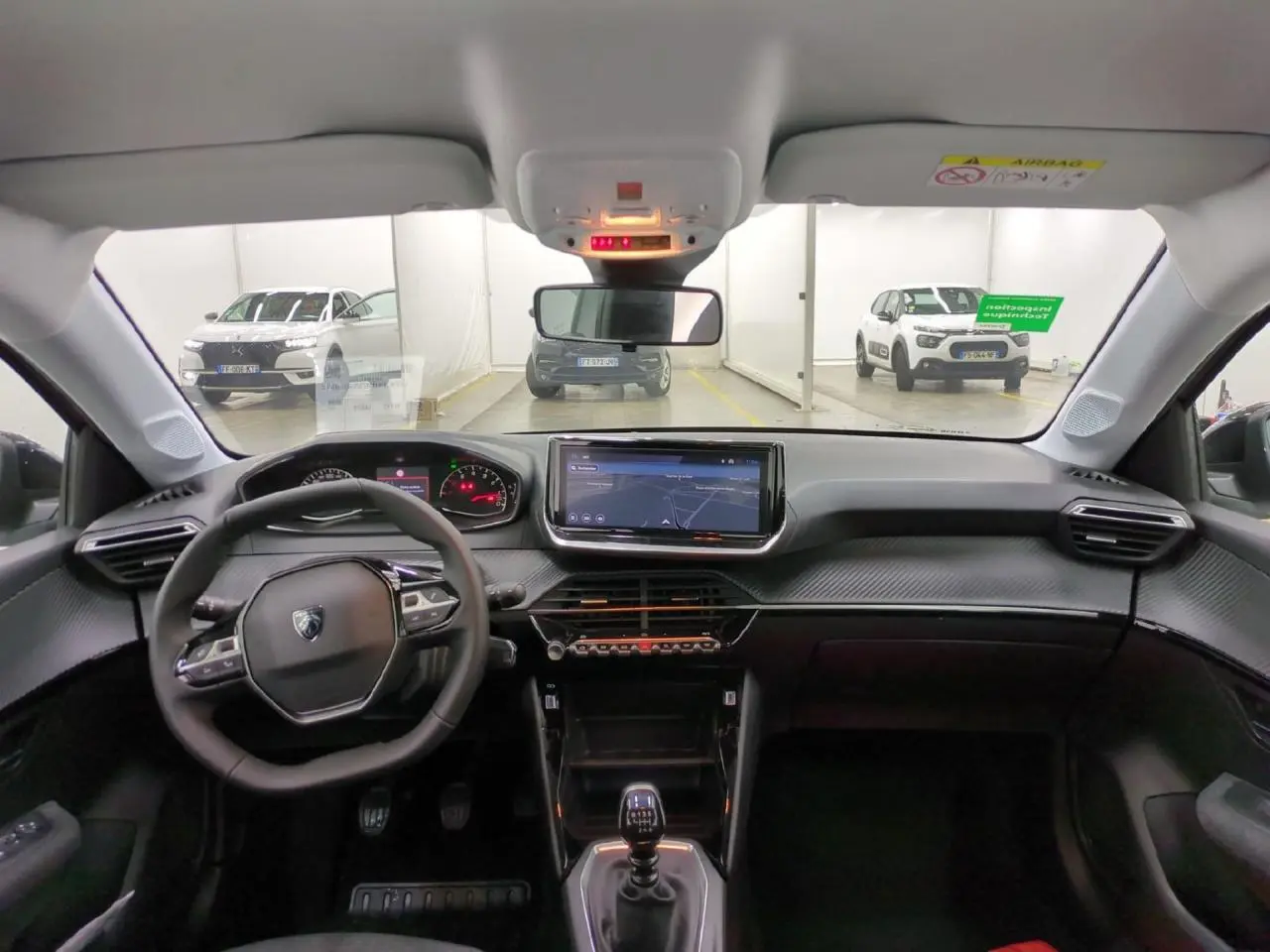 Vue intérieure avant du Peugeot 208 gris clair 2025, avec tableau de bord carbone et écran tactile central 10 pouces.