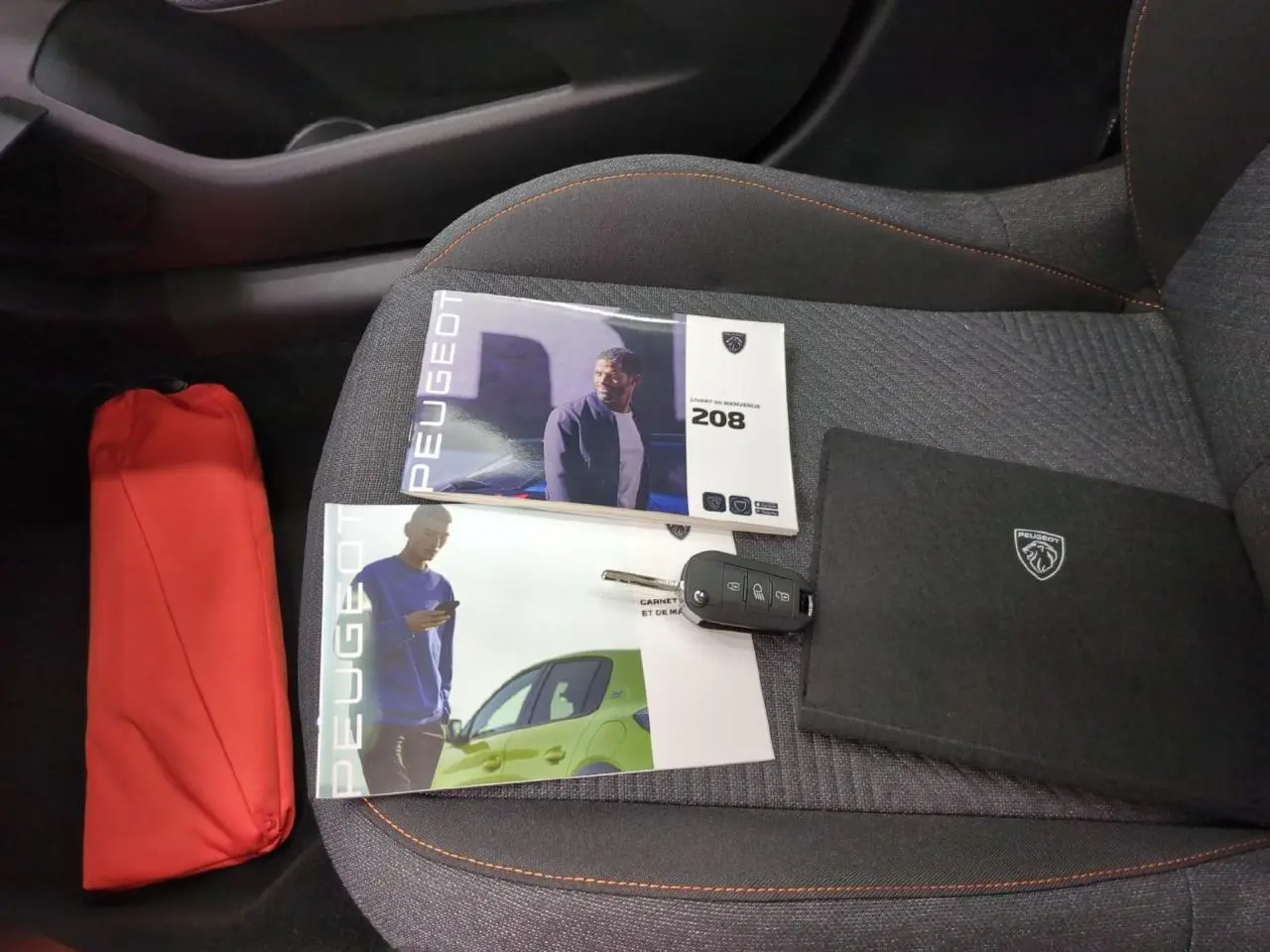 Vue intérieure du siège avant droit gris avec surpiqûres orange, clés et documents Peugeot 208 posés dessus.