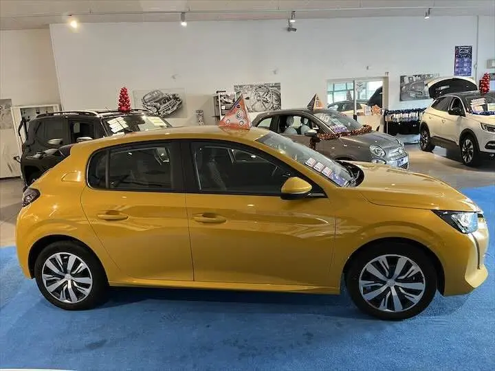 Profil côté gauche d'une Peugeot 208 jaune Faro Metal 2020 exposée en showroom avec des décorations festives sur le toit.