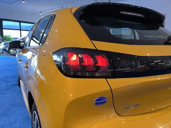 Vue 3/4 arrière gauche d'une Peugeot 208 jaune Faro Metal avec feux arrière allumés dans un showroom.