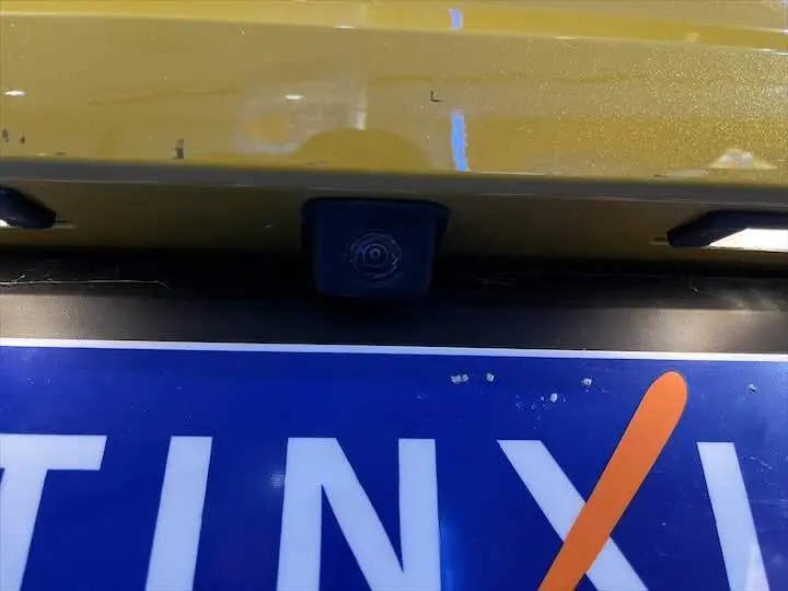 Gros plan sur la caméra de recul noire intégrée au hayon jaune Faro Métal d'une Peugeot 208 2020.