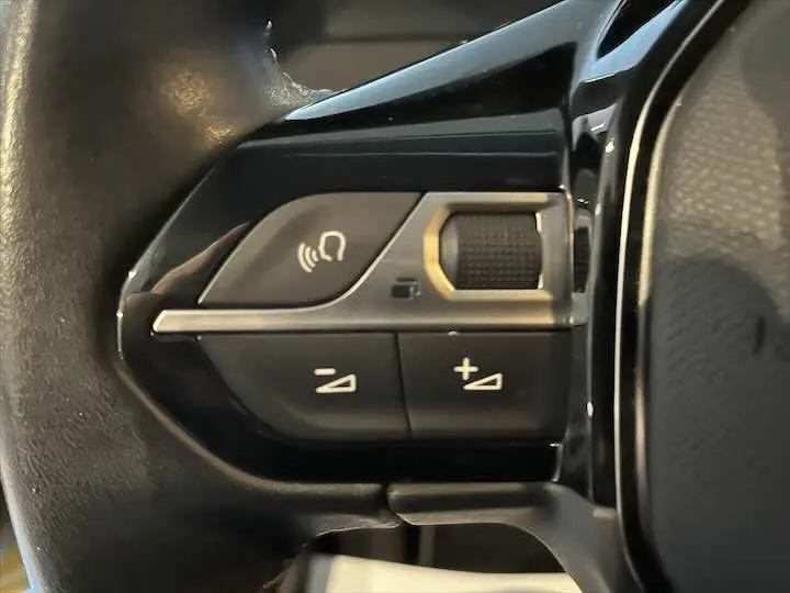 Gros plan sur les commandes de volume et téléphone intégrées au volant noir de la Peugeot 208 jaune Faro Metal.