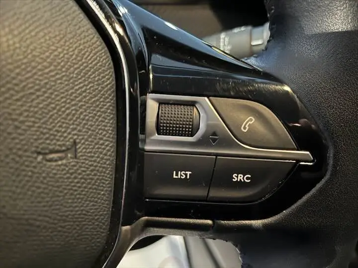 Gros plan sur les commandes au volant noir de la Peugeot 208 diesel, boutons LIST et SRC visibles.