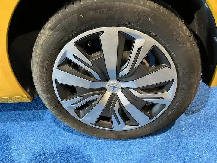 Gros plan sur la roue avant gauche de la Peugeot 208 jaune Faro Metal, avec jante alliage au design moderne.