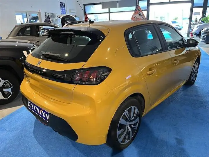 Vue 3/4 arrière droite d'une Peugeot 208 jaune Faro Metal exposée en showroom avec jantes alliage et toit noir contrasté.