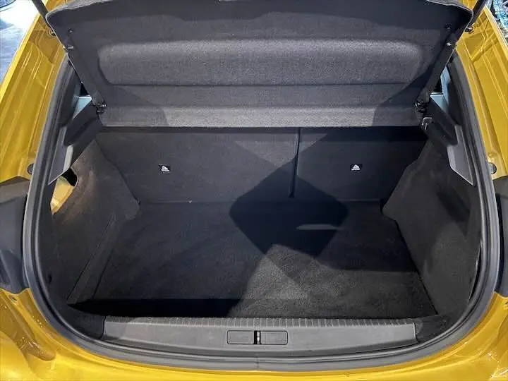 Coffre ouvert vu de l'arrière d'une Peugeot 208 jaune Faro Metal, montrant un espace de chargement propre et vide.