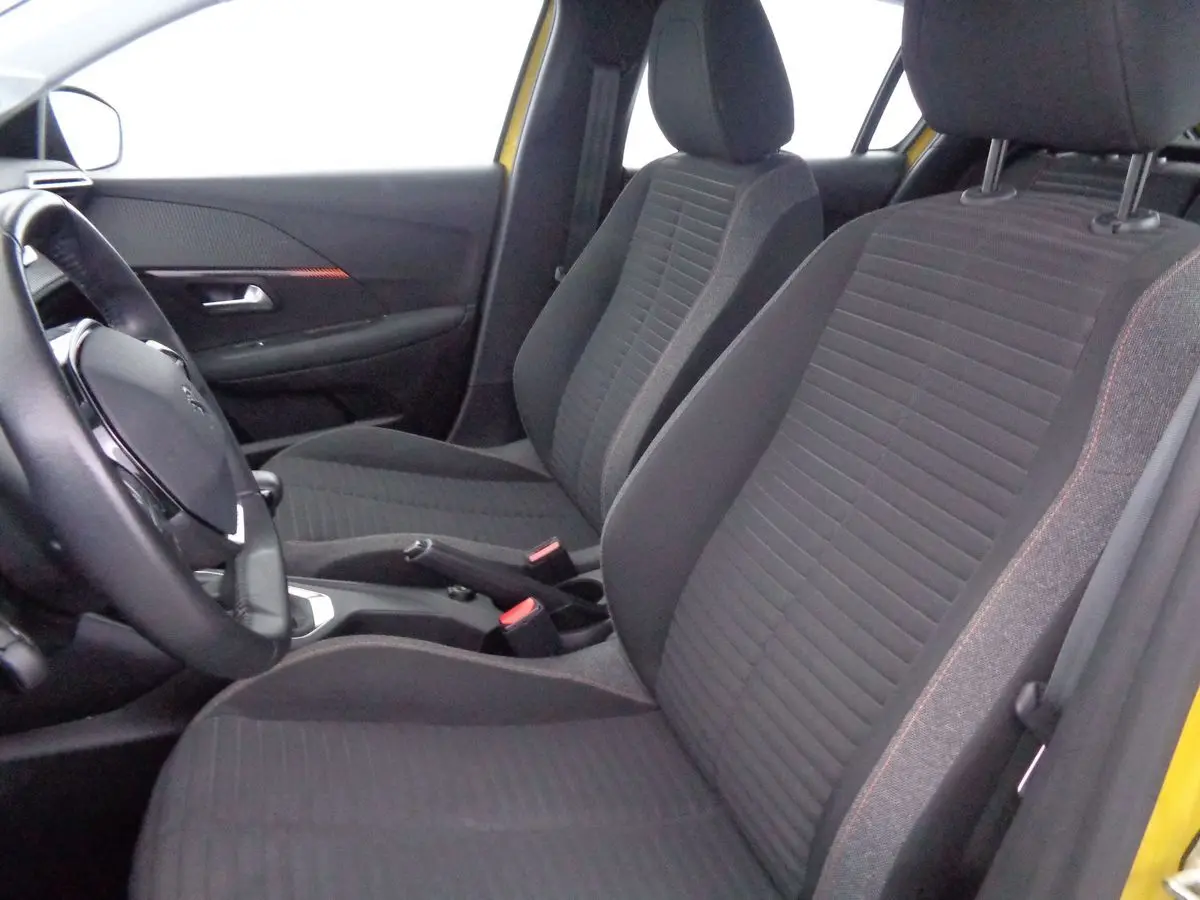 Vue intérieure côté conducteur de la Peugeot 208 jaune Faro Metal, sièges avant en tissu gris avec surpiqûres rouges.