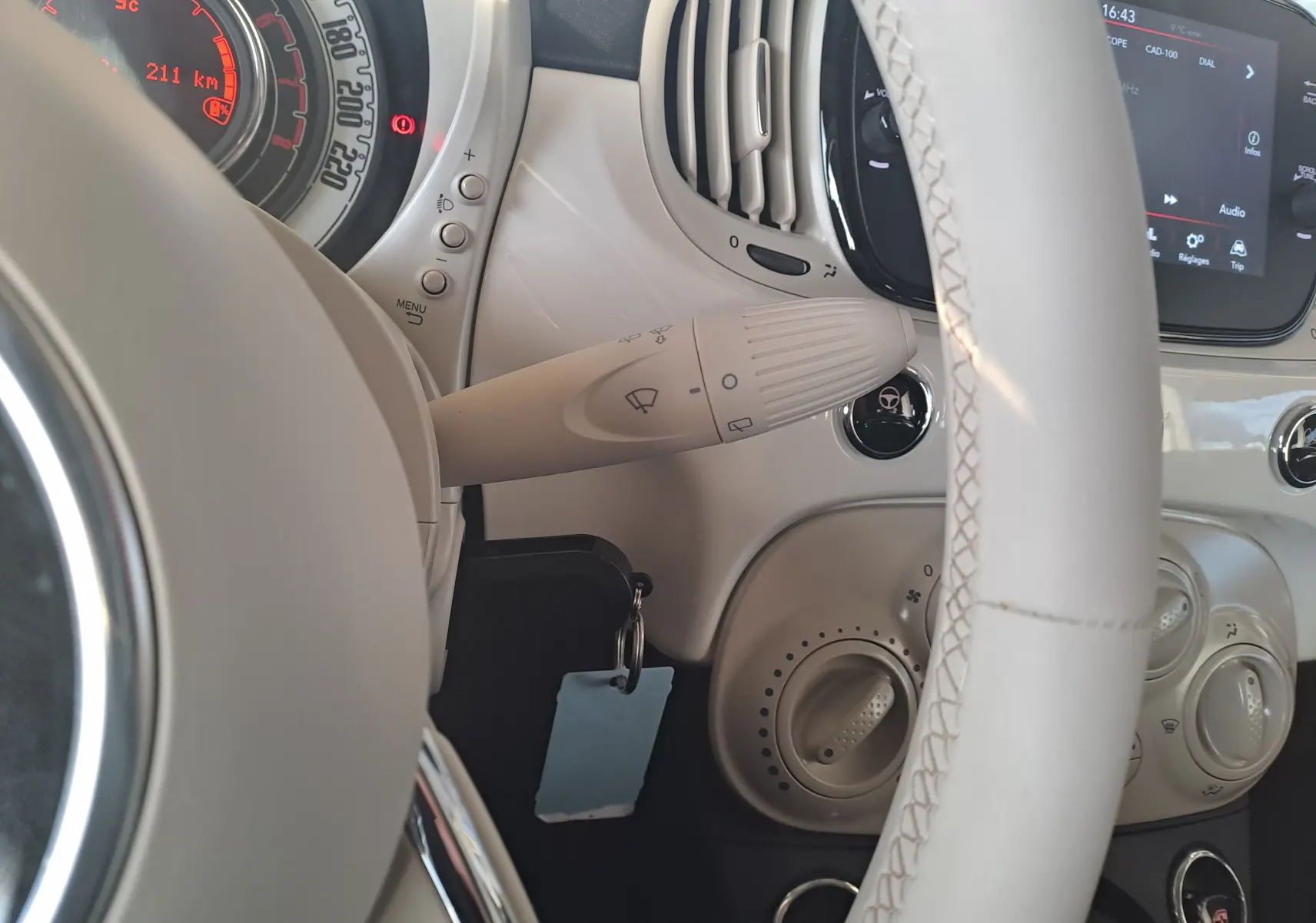 Vue rapprochée du volant blanc et du tableau de bord beige clair de la Fiat 500 2023 avec commandes et écran tactile.