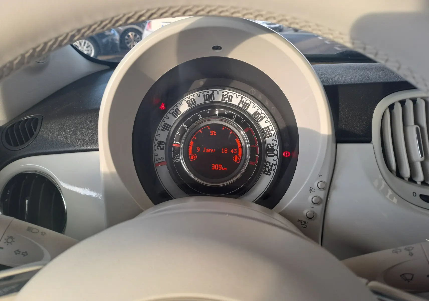 Vue rapprochée du tableau de bord blanc de la Fiat 500 2023, avec compteur circulaire et affichage digital rouge.