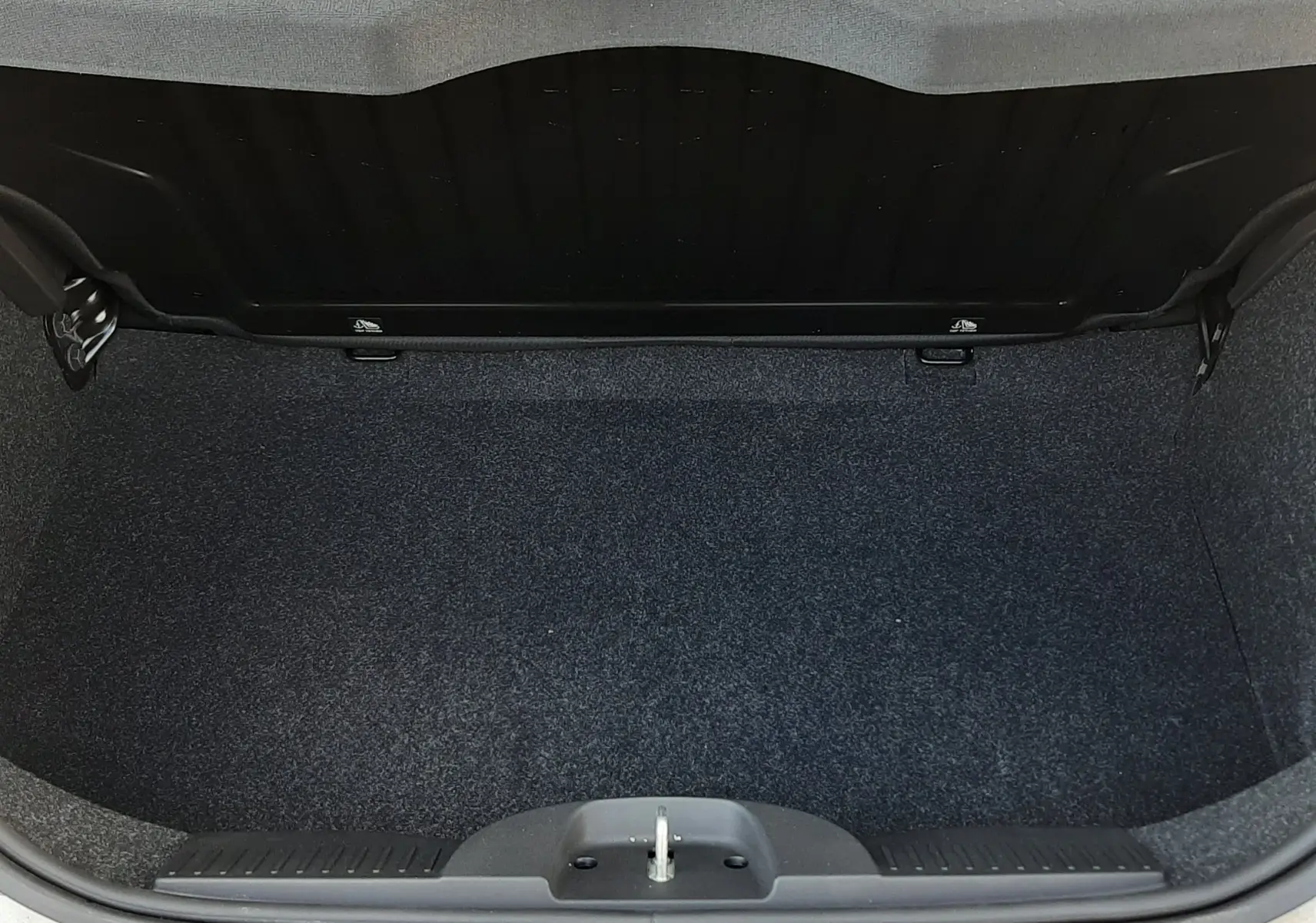 Coffre ouvert vu de dessus d'une FIAT 500 blanche, montrant l'espace de chargement vide et la moquette sombre.