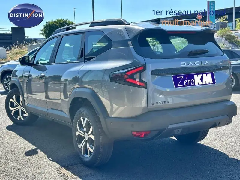 Vue 3/4 arrière droite du SUV Dacia Bigster gris avec feux arrière LED et barres de toit sur parking.