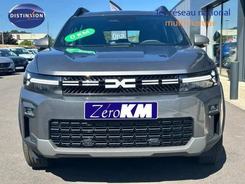 Vue avant du Dacia Bigster gris avec calandre noire et logo central distinctif, en extérieur sur parking.
