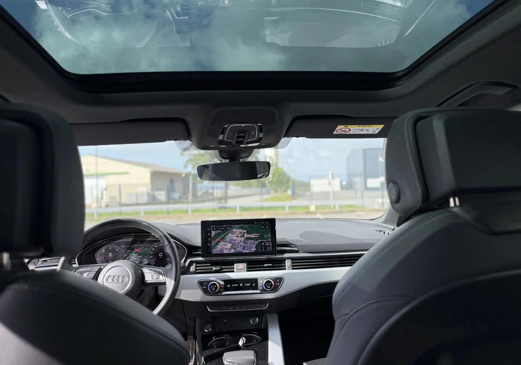 Vue intérieure avant de l'Audi A4 Avant gris Daytona, avec tableau de bord numérique et toit panoramique en verre.