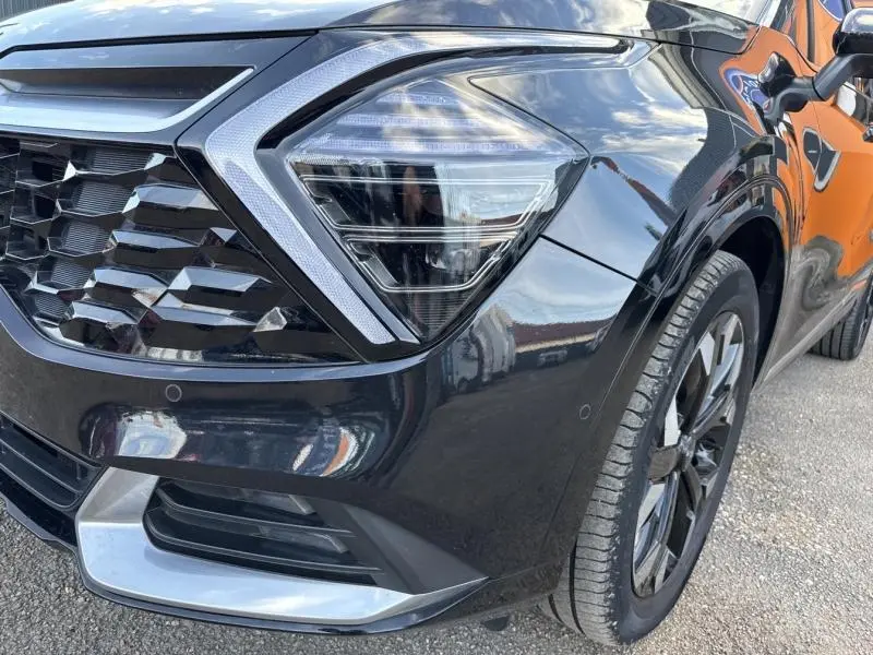 Gros plan sur l'avant droit du KIA SPORTAGE noir Basalte métallisé, mettant en valeur le phare LED et la calandre noire laquée.