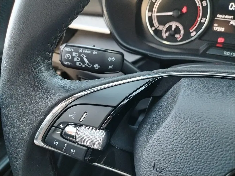 Gros plan sur la commande multifonction gauche du volant noir de la Skoda Fabia 2023, avec molette argentée et tableau de bord partiel.