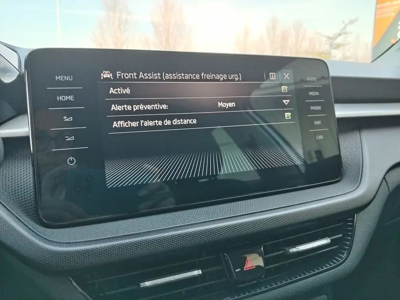 Écran tactile central du tableau de bord de la Skoda Fabia 2023 affichant l'assistance freinage d'urgence Front Assist.