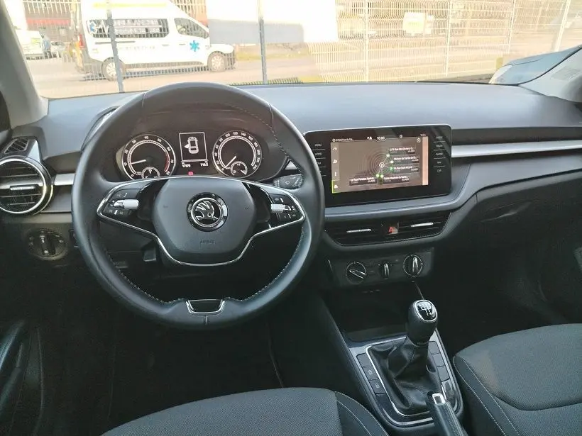 Vue intérieure frontale du poste de conduite d'une Skoda Fabia blanche 2023 avec volant multifonction et écran tactile central.