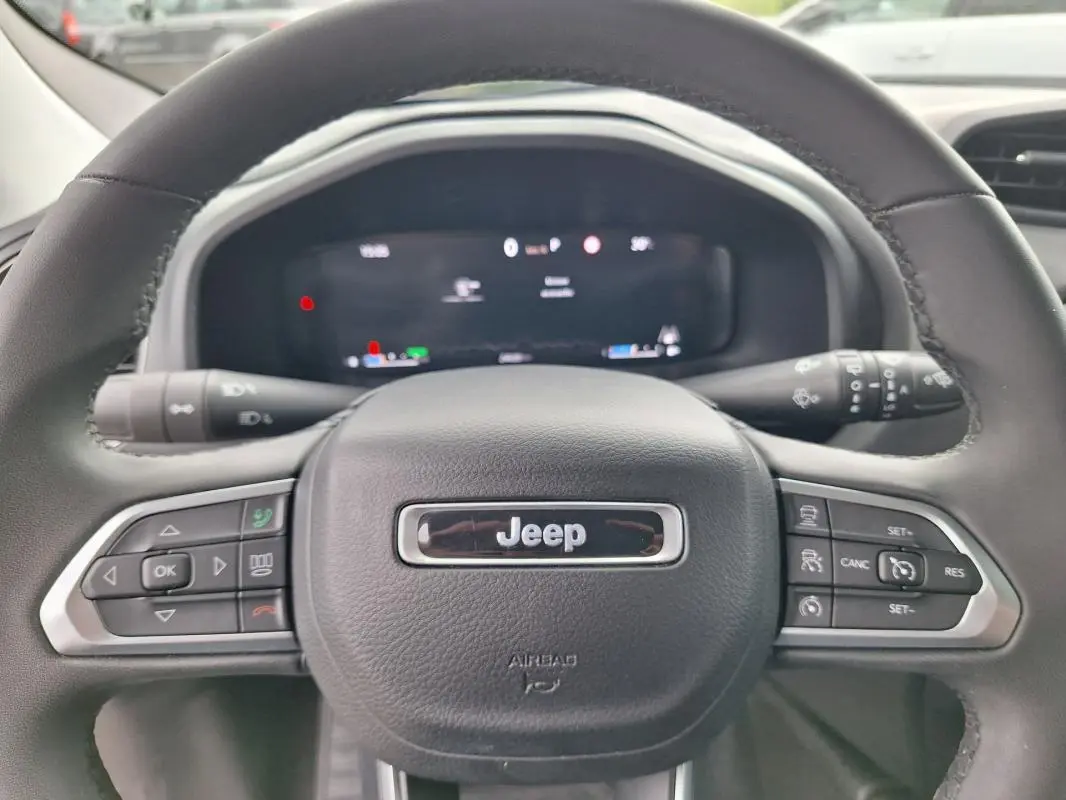 Vue rapprochée du volant Jeep Renegade 2024, noir avec commandes intégrées et tableau de bord numérique flou.