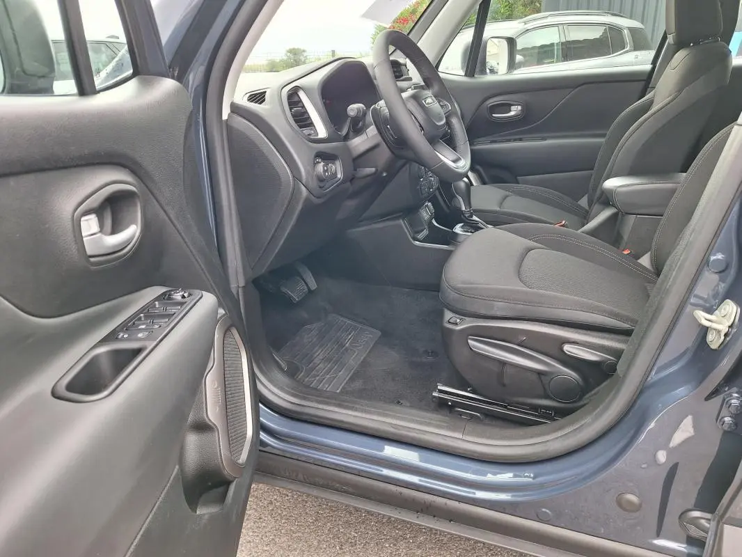Vue intérieure côté conducteur d'un Jeep Renegade bleu 2024, montrant sièges noirs et accoudoir central.