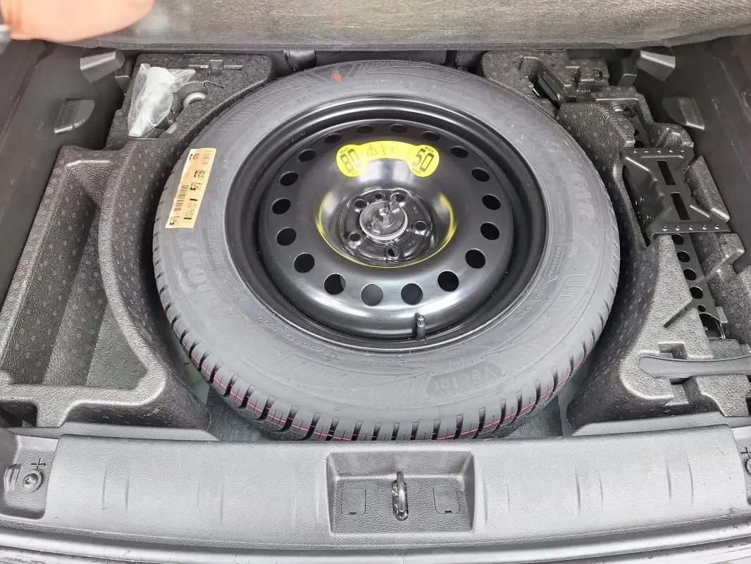 Vue de dessus sur la roue de secours noire dans le coffre du Jeep Renegade bleu 2024, avec outils de bord rangés.