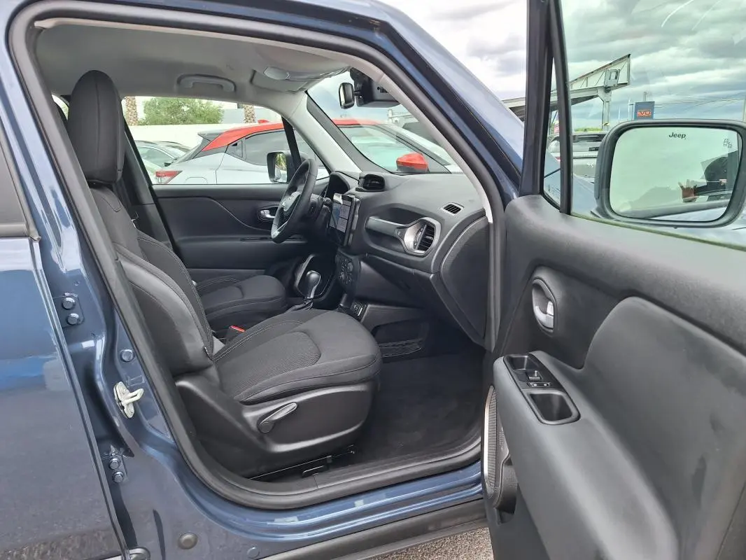 Vue intérieure côté conducteur d'un Jeep Renegade bleu 2024, montrant sièges noirs et tableau de bord avec écran tactile.