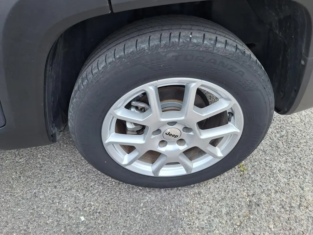 Gros plan sur la roue avant gauche d’un Jeep Renegade bleu 2024 avec jante alliage 17 pouces et logo Jeep au centre.