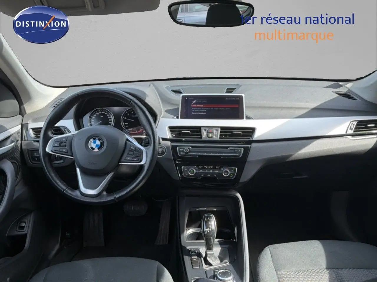 Vue intérieure avant du BMW X1 blanc 2022, mettant en valeur le tableau de bord moderne et le volant multifonction.