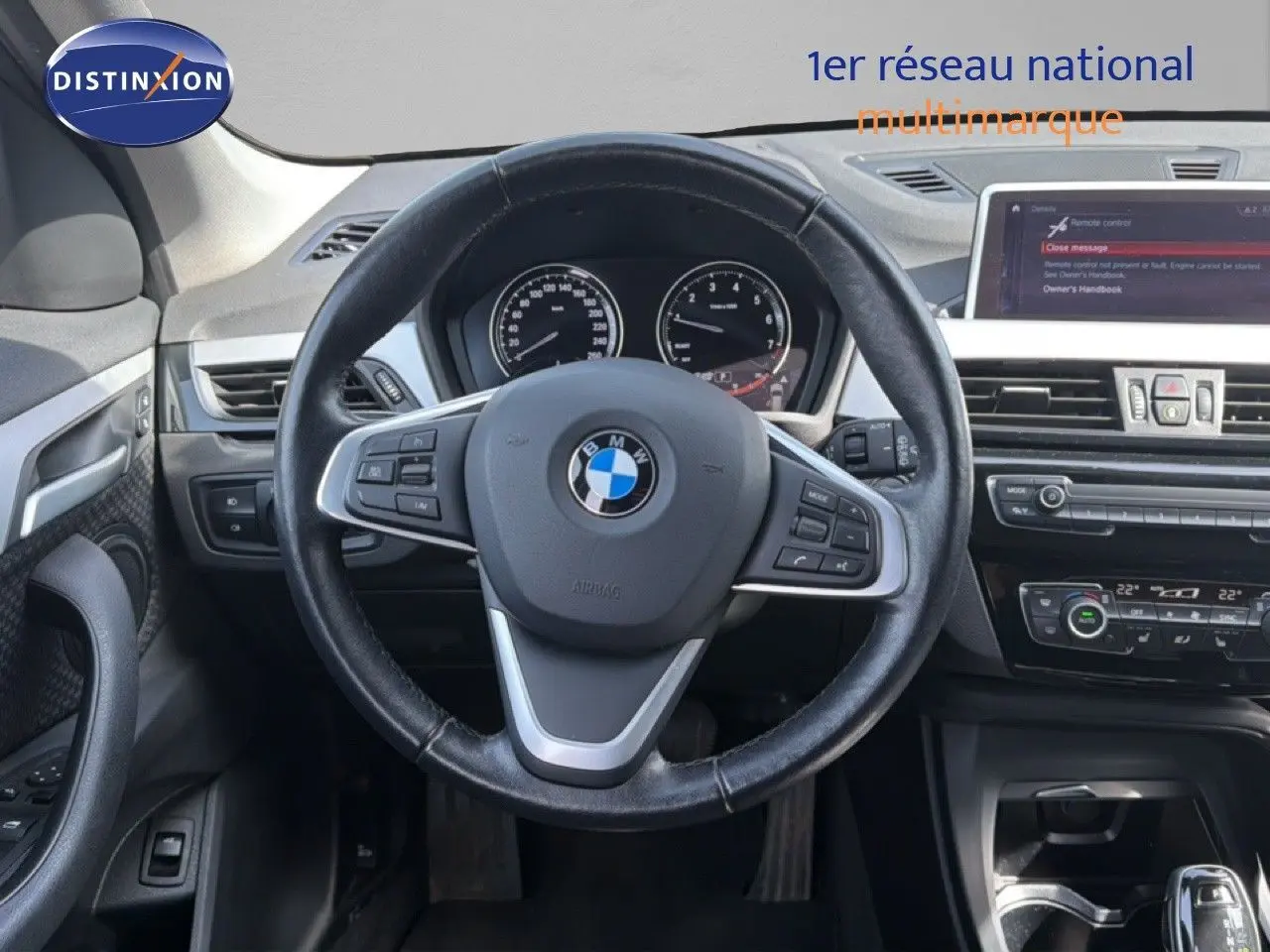 Vue intérieure centrée sur le volant noir d'une BMW X1 2022, avec tableau de bord et écran multimédia visibles.
