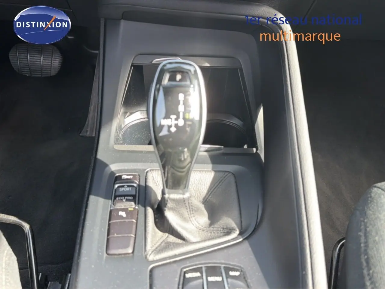 Gros plan sur la console centrale et levier de vitesse automatique d’une BMW X1 blanche, intérieur noir.