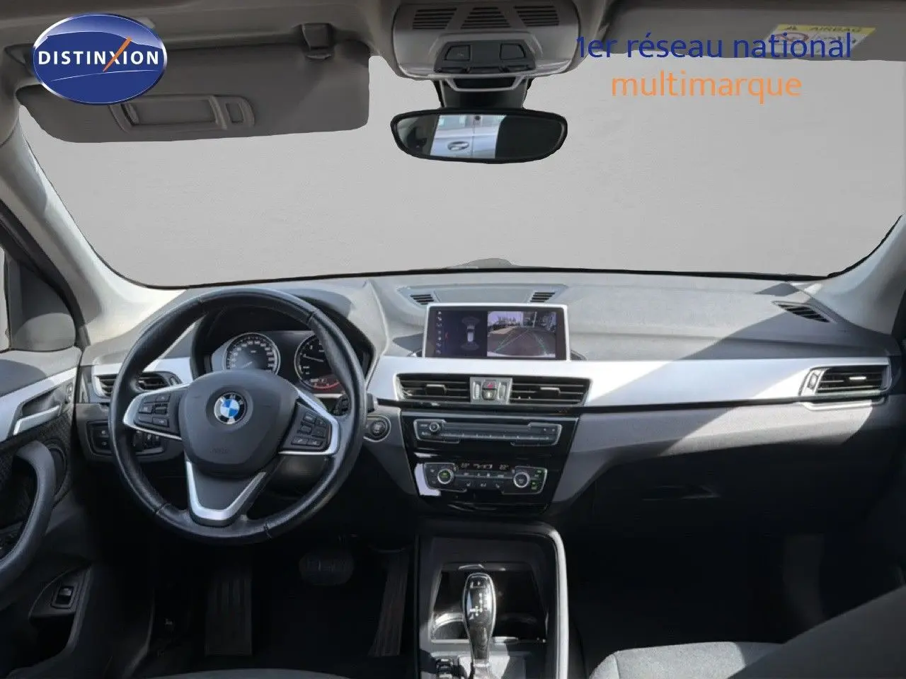 Vue intérieure avant de la BMW X1 blanche 2022, tableau de bord moderne avec écran central et volant multifonction.