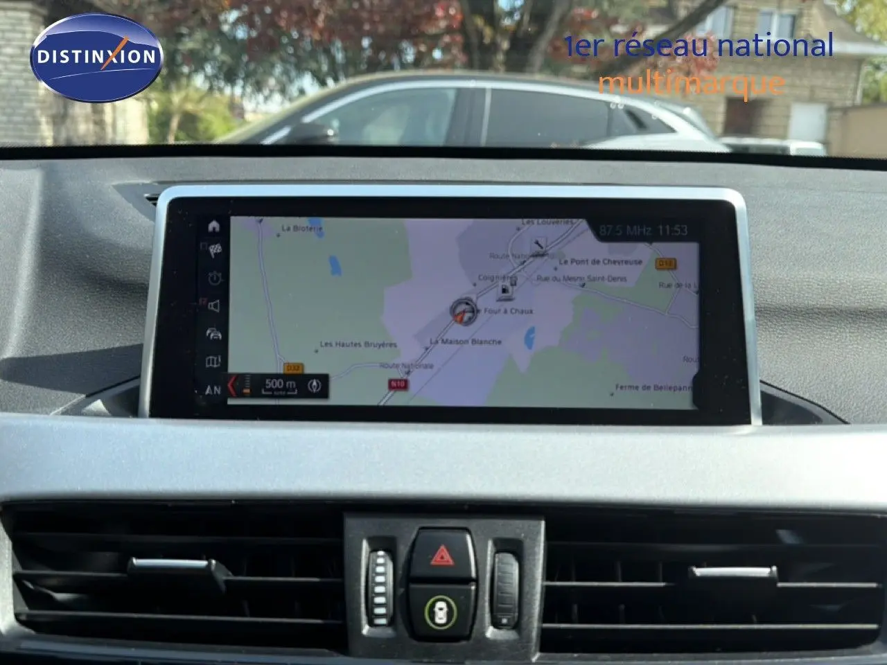 Écran tactile central affichant la navigation GPS dans l'habitacle d'un BMW X1 blanc, vue intérieure frontale.