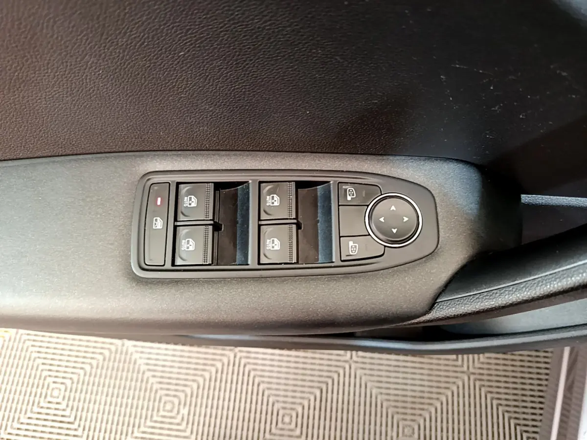 Gros plan sur les commandes des vitres électriques et rétroviseurs sur la porte côté conducteur d’un Renault Captur gris foncé.