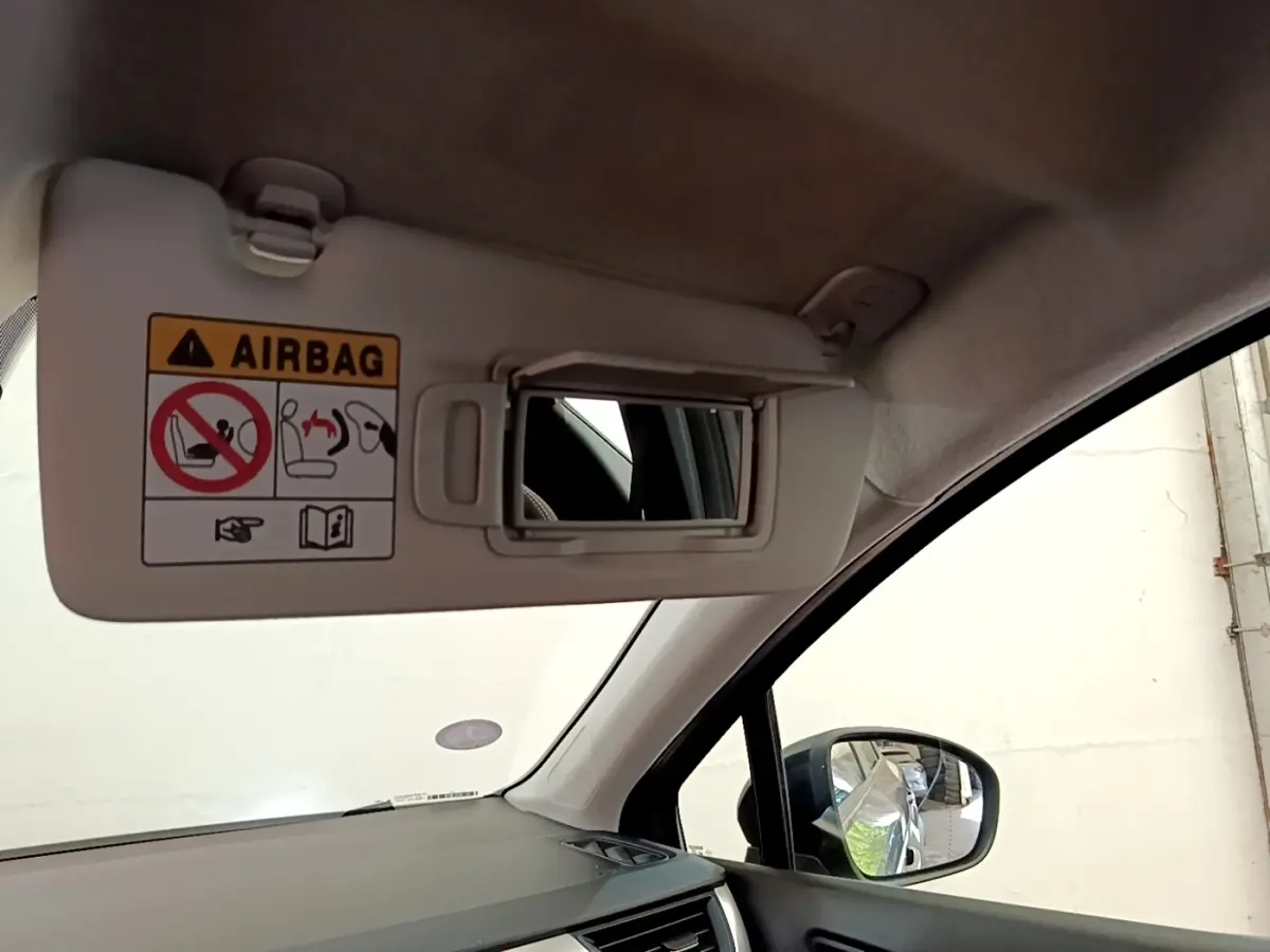 Détail intérieur du pare-soleil côté conducteur avec miroir et avertissement airbag, rétroviseur extérieur noir visible.