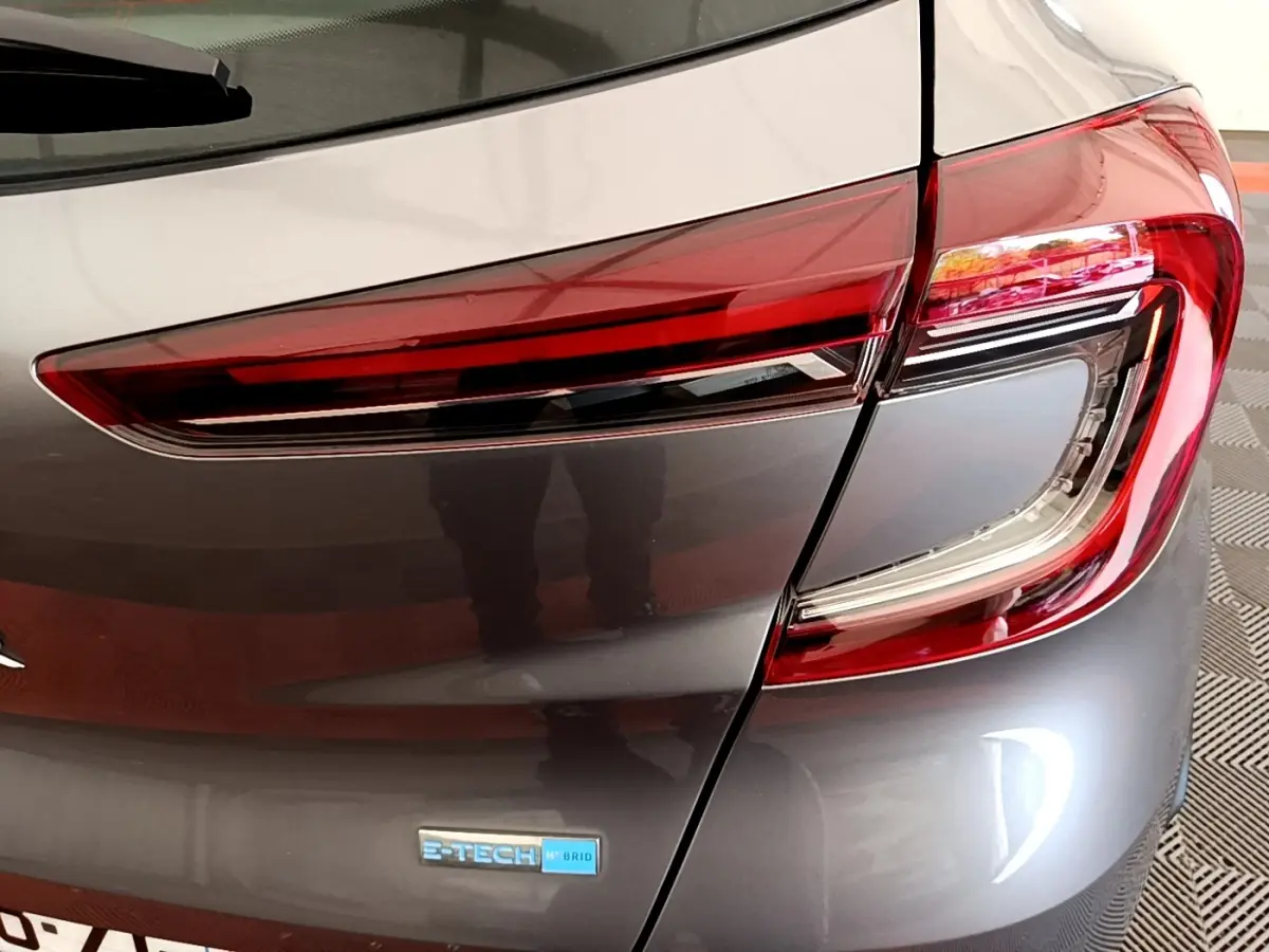 Gros plan sur le feu arrière droit et le logo E-Tech hybride d’un Renault Captur gris foncé 2022.
