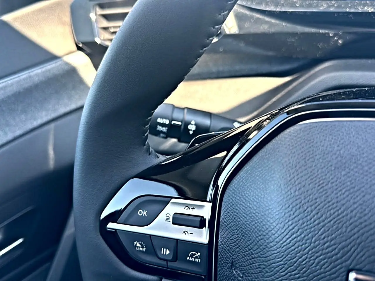 Gros plan sur le volant cuir noir de la Peugeot 408 Hybrid 145 allure, avec commandes intégrées côté gauche.