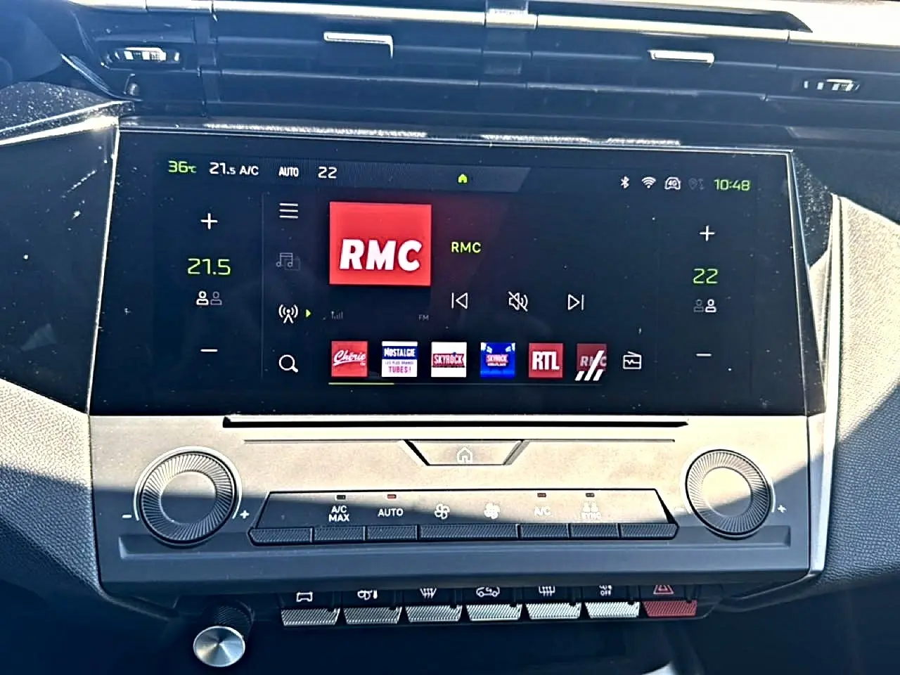 Écran tactile central du tableau de bord du Peugeot 408 Hybrid noir, affichant la radio RMC et commandes climatisation.