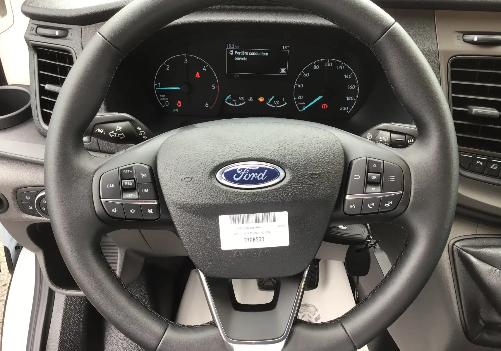 Vue rapprochée du volant noir du Ford Transit Fourgon 2023 avec commandes intégrées et tableau de bord numérique.