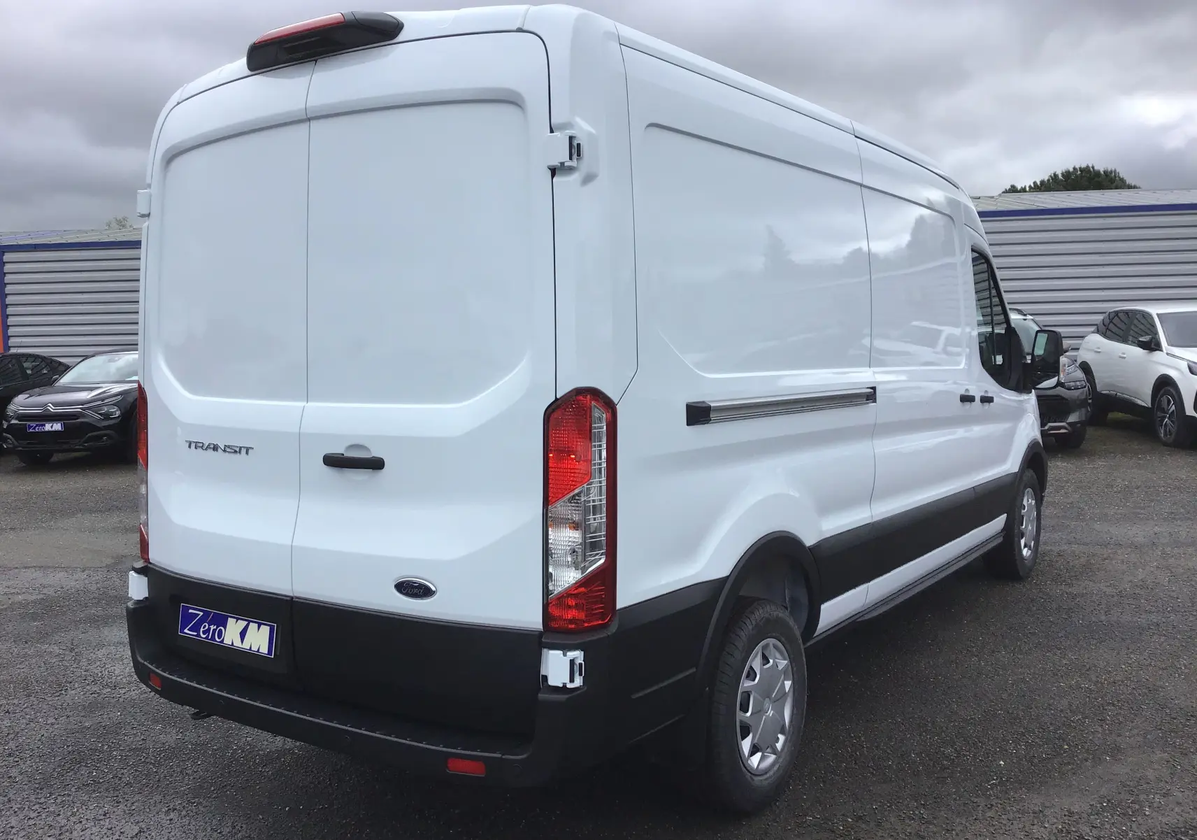 Vue 3/4 arrière droite d'un Ford Transit Fourgon blanc 2023 avec hayon arrière fermé sur parking.